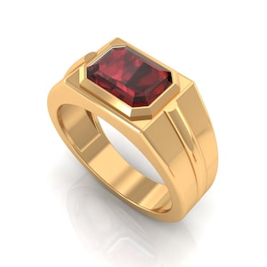 May include: A gold-colored ring with a rectangular, deep red gemstone. The ring has a classic design with a thick band and a geometric setting for the gemstone. The gemstone is faceted, catching the light.