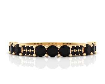 May include: A gold band ring with a repeating pattern of black gemstones. The ring features a series of larger, round stones interspersed with clusters of smaller stones. The ring is set against a white background.