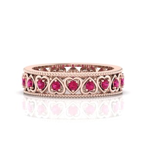 Peut inclure: Une bague en or rose ornée d'un motif de cœurs répétés. Chaque cœur est serti d'une pierre précieuse rose vif. La bague a un bord délicat en perles et une surface polie, reflétant la lumière.