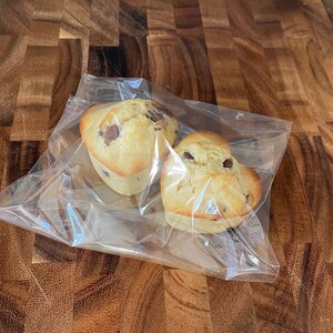 May include: Two heart-shaped chocolate chip muffins wrapped in clear plastic on a wooden cutting board.