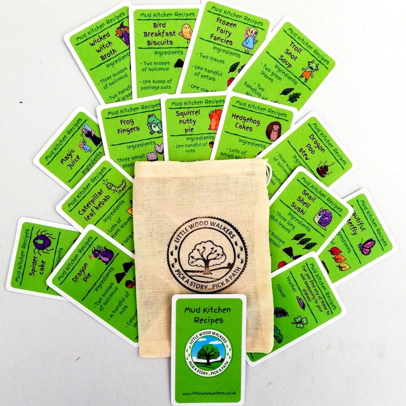 May include: A set of green cards with illustrated recipes for mud kitchen creations. The cards are arranged in a circle around a small, white canvas bag with a brown logo that reads "Little Wood Walkers Pick a Story Pick a Path".