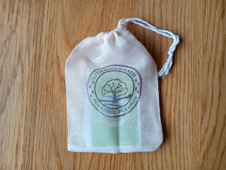 May include: A white cotton drawstring bag with a green and brown logo that says "Little Wood Walkers Pick a Story, Pick a Path".