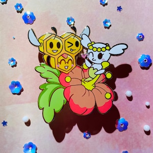 May include: A gold-tone enamel pin featuring a cartoon bee with three faces, a white rabbit with a flower crown, and a pink hibiscus flower.
