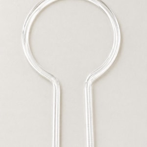 May include: A clear, transparent acrylic plant support stake featuring a circular top loop and two parallel, pointed prongs at the base. The structure is smooth, rigid, and designed with a simple, functional shape for insertion into soil.