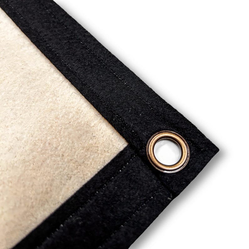 May include: Close-up of a corner of a white backdrop with a black border and a brass grommet.
