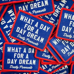 May include: Close-up of multiple blue and red fabric patches with white text that reads "What a day for a day dream" and "Dusty Pennants".