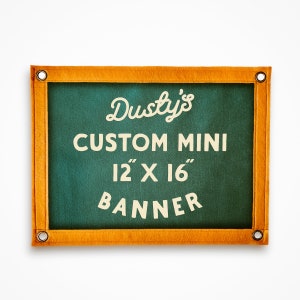 Pode incluir: Uma mini-faixa personalizada de 12" x 16" com fundo verde e borda laranja. O texto "Dusty's Custom Mini 12" x 16" Banner" está impresso em branco.