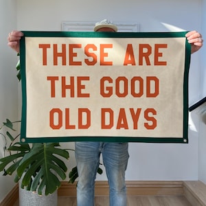 May include: A rectangular banner with the text "THESE ARE THE GOOD OLD DAYS" in orange block letters. The banner has a cream-coloured background with a dark green border.
