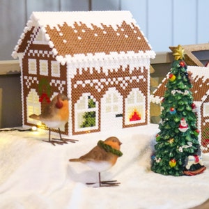 Könnte beinhalten: Eine festliche Weihnachtsdekoration mit Lebkuchenhaus-Dekorationen in Braun und Weiß mit 'Schnee'. Ein kleiner Weihnachtsbaum und dekorative Vögel sind ebenfalls vorhanden und schaffen eine festliche Szene.
