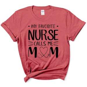 Puede incluir: Camiseta roja con texto negro que dice "Mi enfermera favorita me llama mamá" con un corazón y un estetoscopio.