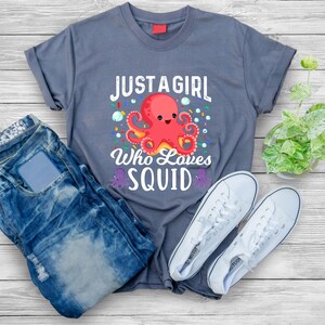 Könnte beinhalten: Ein graues T-Shirt mit dem Text "Just a girl who loves squid" und einem roten Cartoon-Oktopus mit einem lächelnden Gesicht.