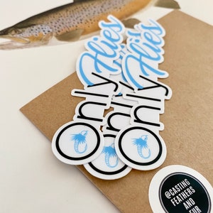 Könnte beinhalten: Ein Satz von fünf weißen Aufklebern mit einem blauen Fliegen-Design und dem Text "Only Flies" in blauer Kursivschrift. Die Aufkleber befinden sich auf einem braunen Papieruntergrund. Es gibt einen kleineren weißen Aufkleber mit schwarzem Text, der "@casting feathers and fur" lautet.