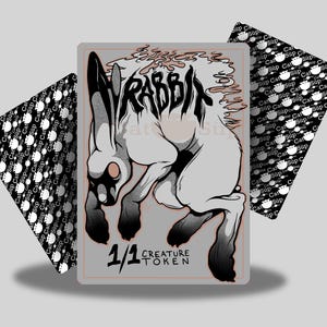 Könnte beinhalten: Fantasiekarte mit einer schwarz-weißen Kaninchenillustration und dem Wort "RABBIT". Die Karte ist mit "1/1 CREATURE TOKEN" beschriftet und wird von zwei Karten mit Muster begleitet.