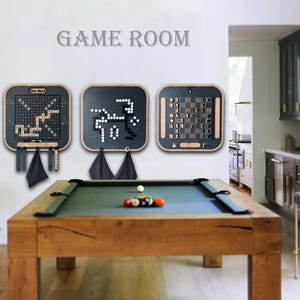May include: Three square wall-mounted game boards featuring a word game, a Go board with black and white stones, and a chess set. The boards have dark frames and light wood accents. Below the boards, a wooden pool table holds billiard balls.