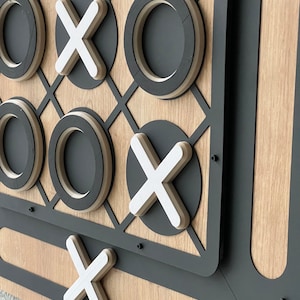 May include: A wooden tic-tac-toe game with black metal trim. The game board has white X's and black O's.