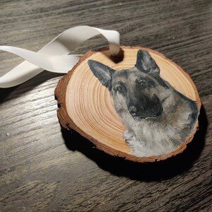 Side angle of a custom hand painted pet portrait on wood slice ornament with white ribbon. Detailed and realistic painted dog portrait. Added text available. German Shepperd.