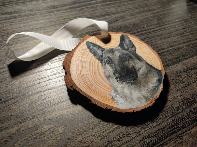 Side angle of a custom hand painted pet portrait on wood slice ornament with white ribbon. Detailed and realistic painted dog portrait. Added text available. German Shepperd.