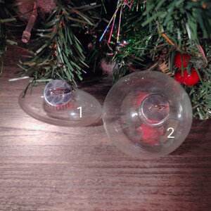 May include: Two clear glass Christmas ornaments with silver tops. The larger ornament is labeled "2" and the smaller ornament is labeled "1".