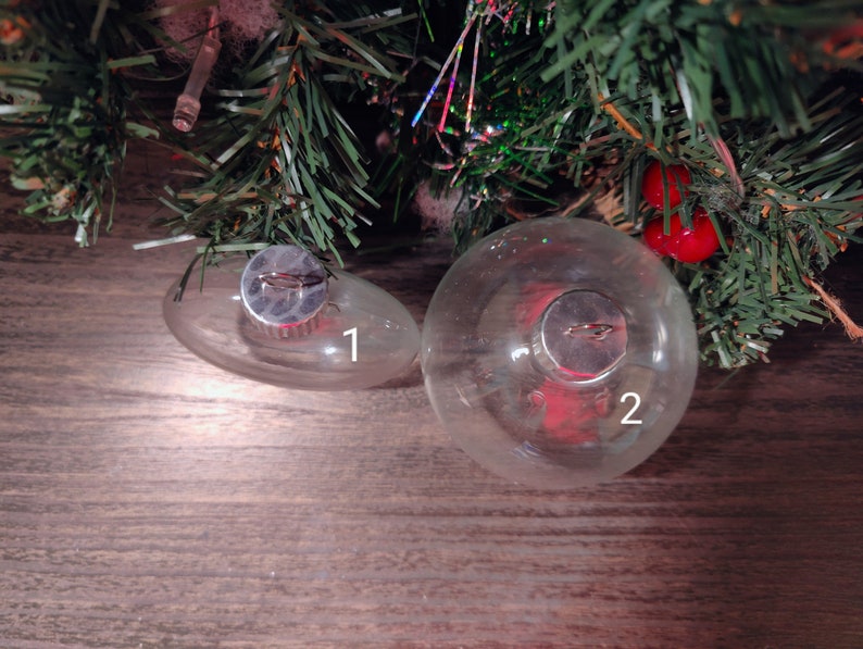 May include: Two clear glass Christmas ornaments with silver tops. The larger ornament is labeled "2" and the smaller ornament is labeled "1".