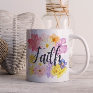 May include: White ceramic mug with a floral design and the word "Faith" in black script. The flowers are pink, yellow, and purple.