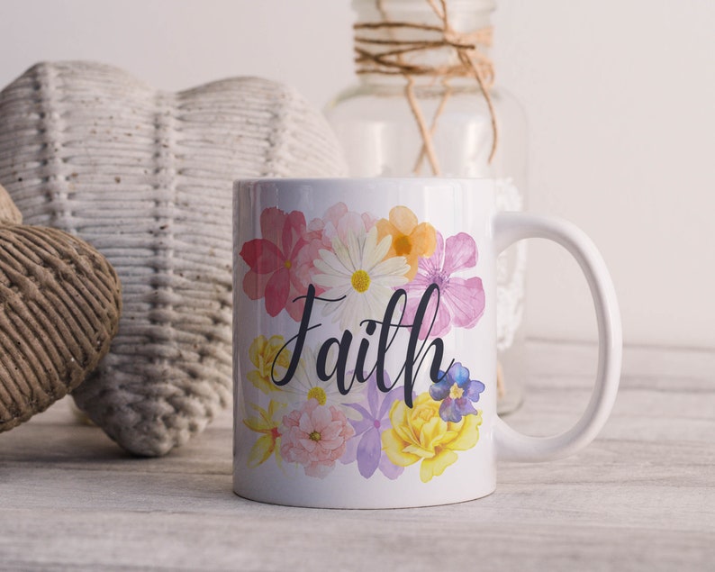 May include: White ceramic mug with a floral design and the word "Faith" in black script. The flowers are pink, yellow, and purple.