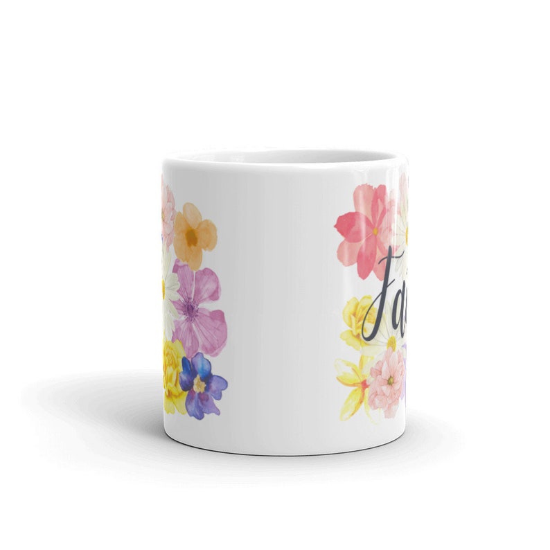 May include: White ceramic mug with a floral design featuring pink, yellow, and blue watercolor flowers. The text "Family" is written in black cursive on the right side of the mug.