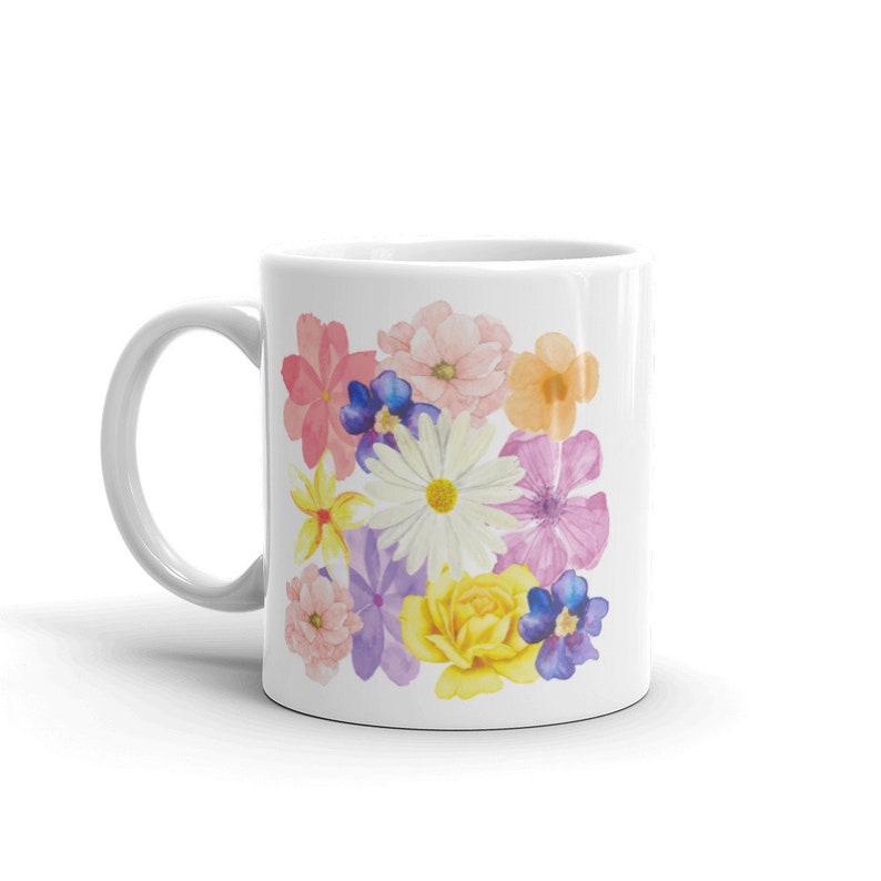 May include: White ceramic mug with a colorful floral design. The design features a variety of flowers in shades of pink, purple, yellow, and blue.