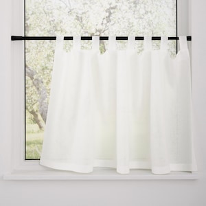 Puede incluir: Una cortina blanca con trabillas cuelga de una fina barra de tensión negra instalada horizontalmente en el marco de una ventana. La tela es semitransparente y cuenta con una serie de trabillas espaciadas uniformemente en la parte superior que se deslizan sobre la barra, creando suaves pliegues verticales.