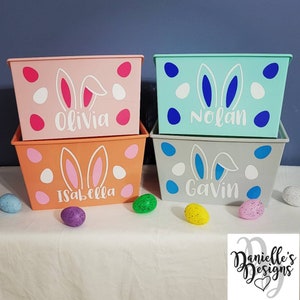 May include: Four pastel colored plastic storage bins with bunny ears and white polka dots. The bins are stacked in pairs and labeled with the names Olivia, Isabella, Nolan, and Gavin.