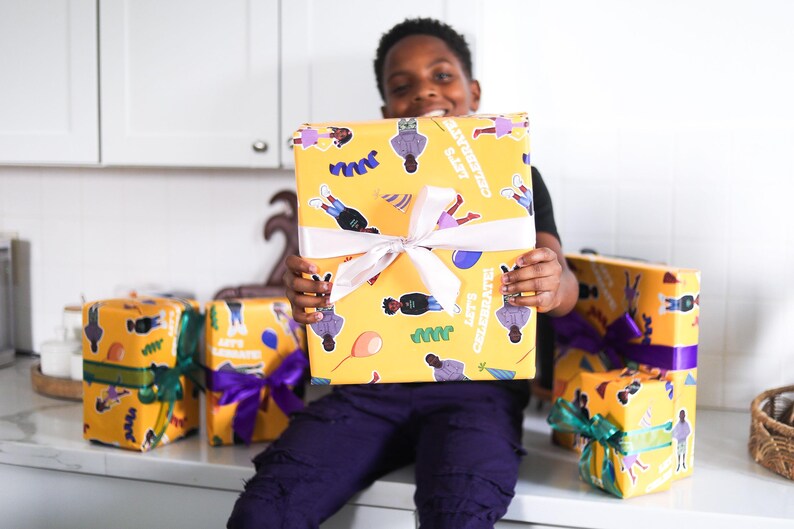 May include: A young person holds a large, yellow gift box wrapped in patterned paper with the words "LET'S CELEBRATE!" and illustrations. Several other wrapped gifts with colorful ribbons are visible.