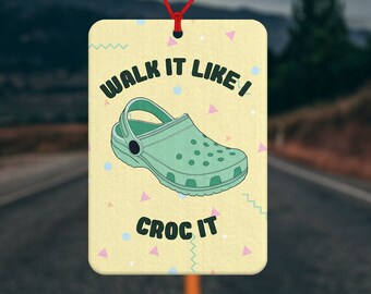 May include: A yellow car air freshener with a green and white cartoon shoe and the text "Walk it like I Croc it".