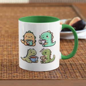 May include: White ceramic mug with a green rim and handle. The mug features four illustrations of cartoon dinosaurs drinking tea or coffee. The text "Tea-Rex" is printed on the mug.
