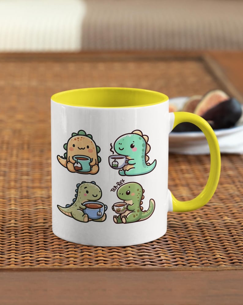 May include: A white ceramic mug with a yellow rim and handle. The mug features a cartoon illustration of four dinosaurs drinking tea. The text "Tea-Rex" is printed on the mug.