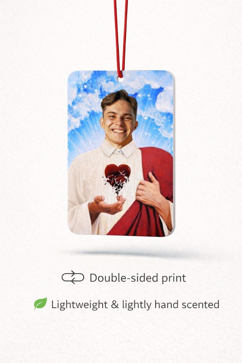 May include: Rectangular air freshener featuring a smiling person in a white shirt and red drape, a broken heart graphic, and a blue sky background. The air freshener has a red string for hanging. Text reads "Double-sided print" and "Lightweight & lightly hand scented."