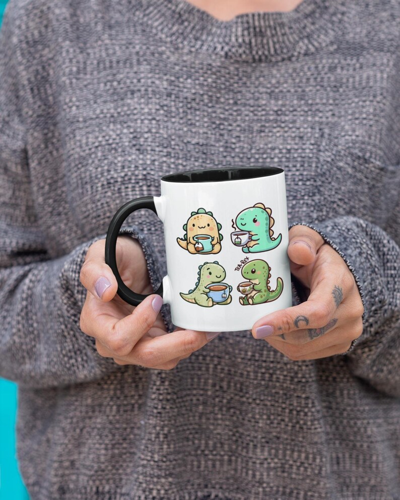 May include: White ceramic mug with a black rim and handle. The mug features a cartoon illustration of four green dinosaurs drinking tea. The text "Tea Rex" is printed on the mug.