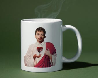 May include: White ceramic mug with a colorful image of a person with a broken heart. The person is wearing a red robe and has a serious expression.