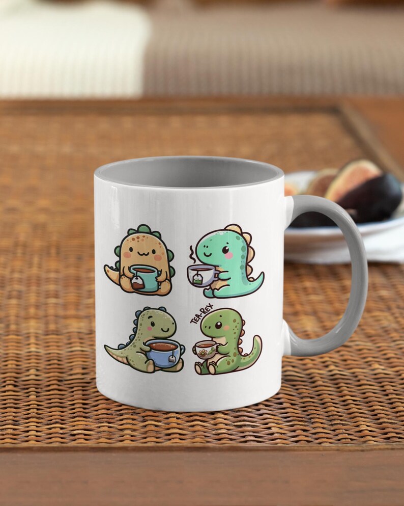 May include: A white ceramic mug with a gray rim and handle. The mug features a cartoon illustration of four dinosaurs drinking tea. The text "Tea Rex" is printed on the mug.
