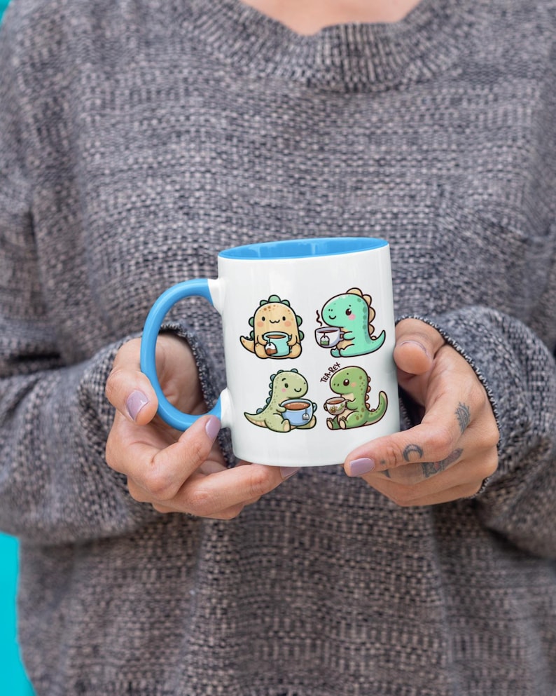 May include: White ceramic mug with a blue rim. The mug features a cartoon illustration of four dinosaurs drinking tea. The dinosaurs are green and yellow.