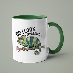 May include: White ceramic mug with a green rim and handle. The mug features a cartoon chameleon with the text "Do I look impressed...?" printed on it.