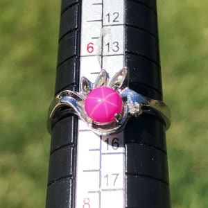 May include: A silver ring with a pink star-shaped gemstone set in a floral design. The ring is sized on a ring sizer that shows a size 8.