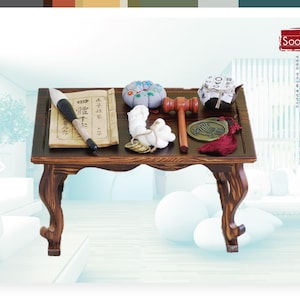 May include: A dark wooden table with a carved design on the legs. The table is set with a book, a brush, a small cushion, a wooden mallet, a coin, and a red tassel. The table is labeled "Soo-A".