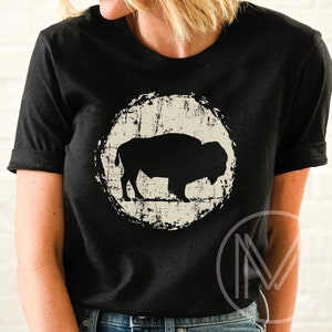 May include: A black t-shirt with a distressed white circle graphic featuring a silhouette of a buffalo. The graphic is centered on the shirt.