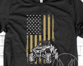 Könnte beinhalten: Dunkelgraues T-Shirt mit einem verblassten amerikanischen Flaggen-Design in Gold und Weiß. Eine weiße Grafik eines Geländewagens befindet sich unter der Flagge. Das T-Shirt hat den Text "MIDWEST MINDS" unten rechts.