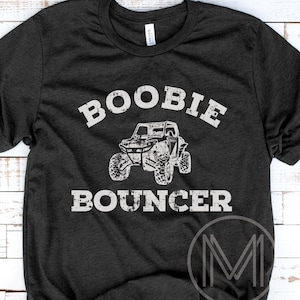 May include: Dark gray t-shirt with the words "BOOBIE BOUNCER" in a distressed white font above a graphic of an off-road vehicle. The shirt also features the "Midwest Minds" logo.