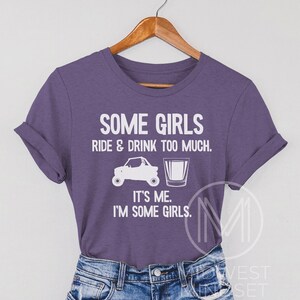 May include: Purple t-shirt with white text that reads "Some girls ride & drink too much. It's me. I'm some girls."  The shirt features a white silhouette of an ATV and a shot glass.