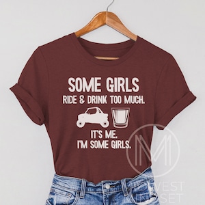 May include: A maroon t-shirt with white text that reads "Some girls ride & drink too much. It's me. I'm some girls."  The text is accompanied by a graphic of a side-by-side vehicle and a shot glass.