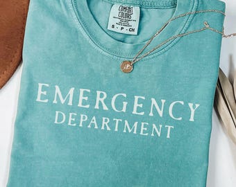 May include: A teal blue t-shirt with the text "EMERGENCY DEPARTMENT" printed in white on the front. The shirt is made of a soft, comfortable material and has a relaxed fit.