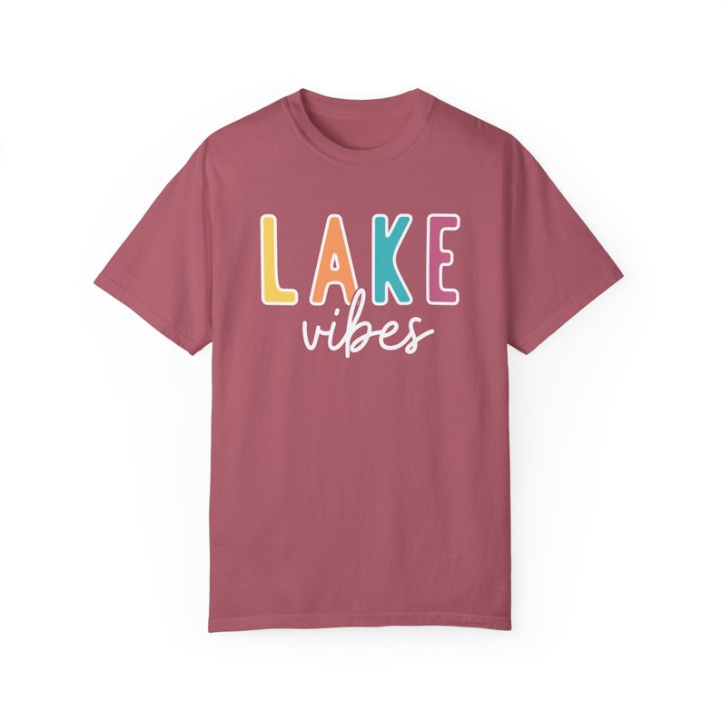 Puede incluir: Una camiseta granate con las palabras "LAKE vibes" impresas en la parte delantera. La palabra "LAKE" est&aacute; en letras de bloque grandes y coloridas, y "vibes" est&aacute; en una fuente cursiva. La camiseta es de material suave.