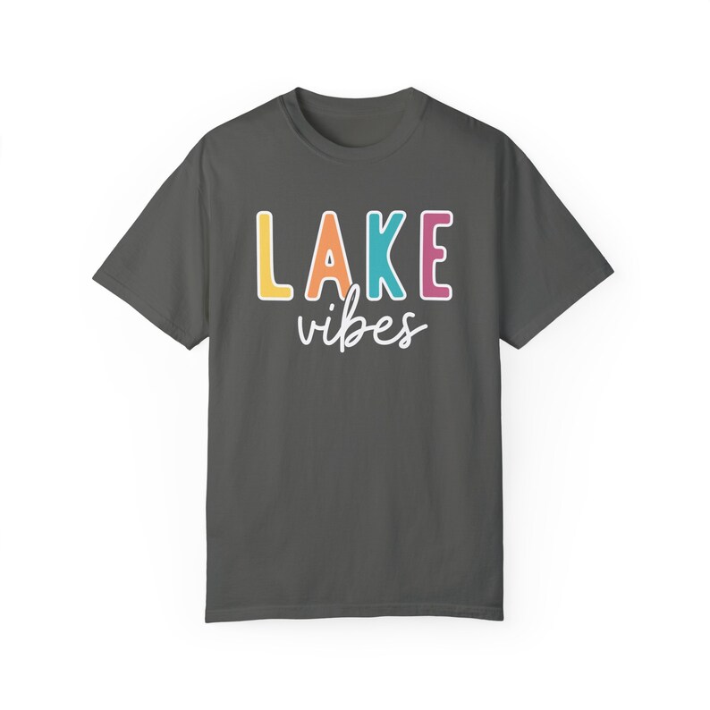 Puede incluir: Camiseta gris oscuro con las palabras "LAKE vibes" impresas. La palabra "LAKE" est&aacute; en letras grandes y coloridas, y "vibes" est&aacute; escrita en cursiva. La camiseta es de estilo casual.