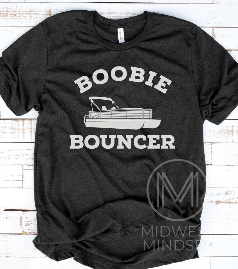May include: A dark gray t-shirt with the text "Boobie Bouncer" in white. A white silhouette of a pontoon boat is below the text. The text "MIDWEST MINDSET" is in white on a black M logo in the lower right corner.
